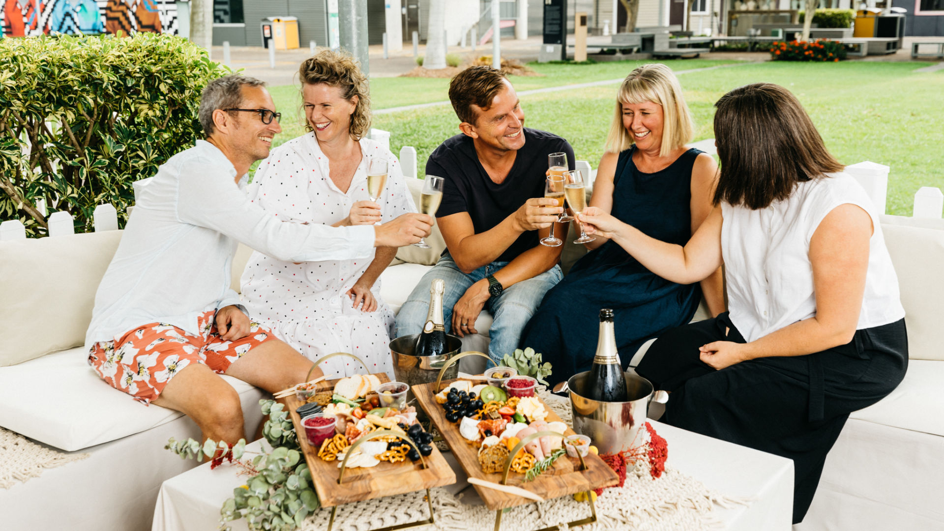 4 people sitting together talking and smiling with champagne in their hands, and a cheese board on the table in front of them