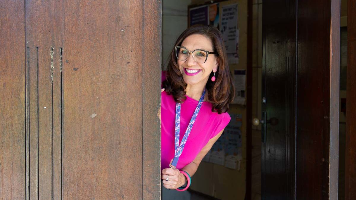 Anita Heiss peeking around the corner of a wall, smiling at camera