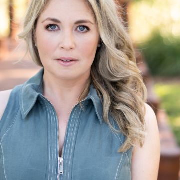 Woman with long blonde curled hair, standing outside, looking at camera