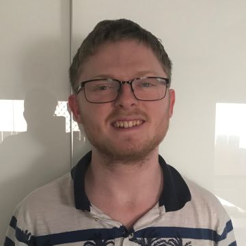 Man with short strawberry blonde hair and glasses smiling at camera