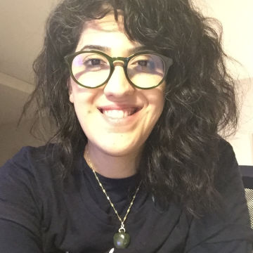 Woman with dark curly hair and glasses smiling at camera