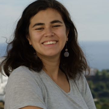Woman with mid-length brown hair, standing outside, smiling at camera