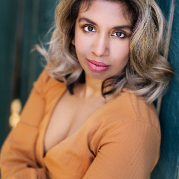 Woman wearing an orange shirt with blonde curled hair looking up to the camera