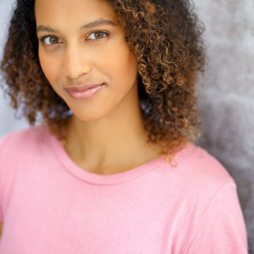 Woman with curly hair and pink shirt looking at the camera and smiling