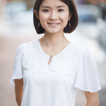 Woman with short brown hair and white shirt standing outside and smiling at camera