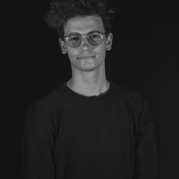 Black and white image of a man smiling to camera wearing a black shirt and glasses