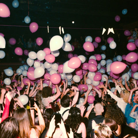 People at party with pink & white balloons falling on them