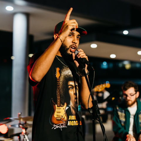 Man on stage speaking into microphone with one hand in the air pointing up