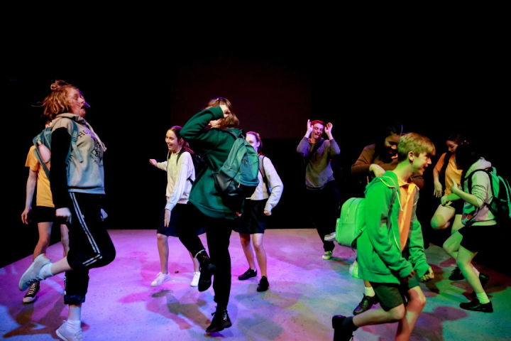 A photo of a student drama production, called RIOT, at La Boite Theatre. Approximately nine drama students are dancing around in celebration at the end of their school drama production, led by La Boite Theatre.  La Boite's In-School workshops give student